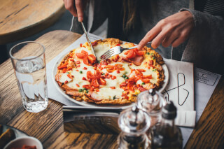 A person enjoys a pizza with a glass of water at a wood table in a restaurant.