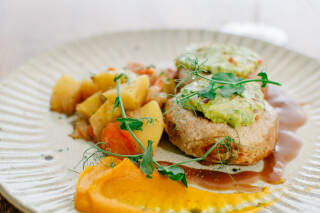 A culinary creation featuring tender meat topped with guacamole, complemented by potatoes and a vibrant orange puree.