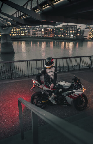 A motorcyclist in full gear pauses on a Yamaha bike against a cityscape backdrop at night.