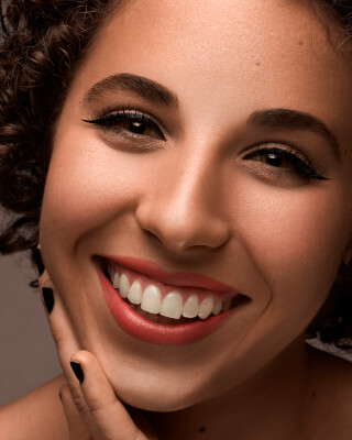 Close-up of a smiling woman with curly hair, showcasing perfect teeth and radiant skin, ideal for beauty and dental care advertising.