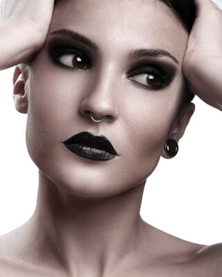Portrait of a woman with dark makeup and a nose ring against a white background.