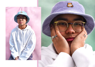 A stylish man wears a bucket hat and glasses in a close-up portrait against a split pink and green background.