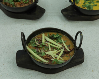 A bowl of daal is garnished with ginger and cilantro. It is placed on a dark wooden surface.