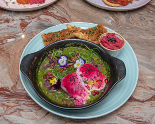 A colorful dish with poached eggs, beetroot, toast, and edible flowers on a blue plate.