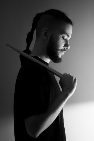 A bearded man in black and white holds drumsticks, creating a moody portrait for musical and artistic themes.