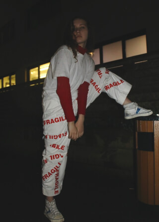 A woman poses in unique fashion with 'fragile' text on her pants at night.
