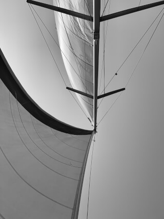 A black and white low angle captures a sailboat's mast and sails against a clear sky, embodying serenity.