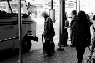 A man stands on a city sidewalk next to a U.S. Postal Service truck in a black and white photograph.