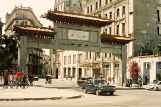 A Chinatown street scene shows classic cars and people under an archway in an old city.