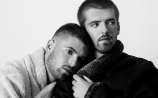 An intimate black and white portrait of a gay couple embracing in a studio setting, showcasing love and affection.