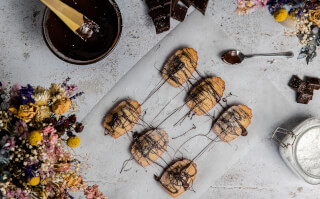 Delicious chocolate madeleines are beautifully arranged with chocolate sauce and flowers for a warm and inviting treat.