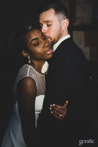 A bride and groom share an intimate moment, the groom kissing the bride's forehead in a tender embrace.