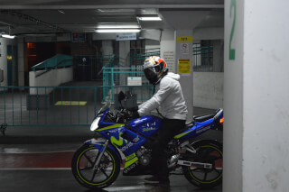 A motorcyclist sits atop his blue motorcycle in an underground parking garage.
