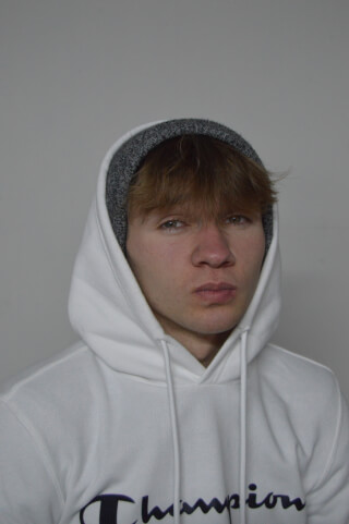 Portrait of a young man wearing a white Champion hoodie and gray beanie against a neutral background.