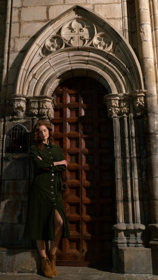 A woman in a green dress stands in front of an old wooden door with arched stone entrance.
