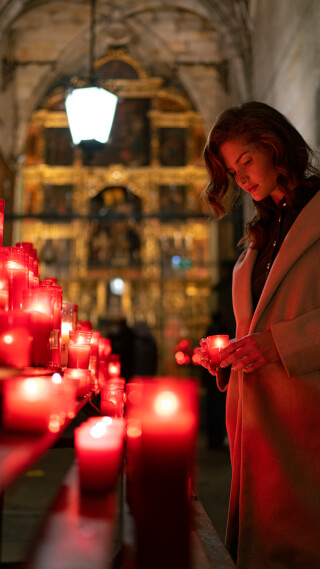 Woman lighting candles in church, creating a serene and spiritual atmosphere.
