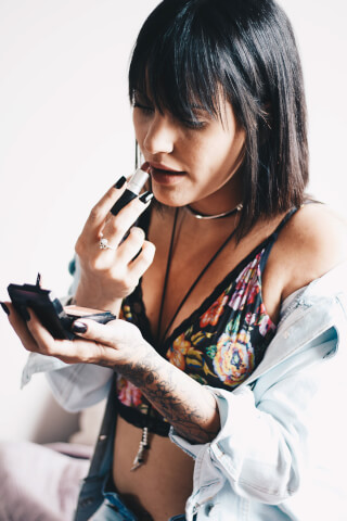 A woman applies lipstick with a modern floral top and denim jacket for a beauty or fashion editorial.