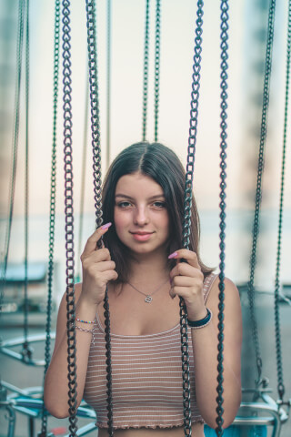 A smiling young woman enjoys a ride at the carnival, holding onto the chains.