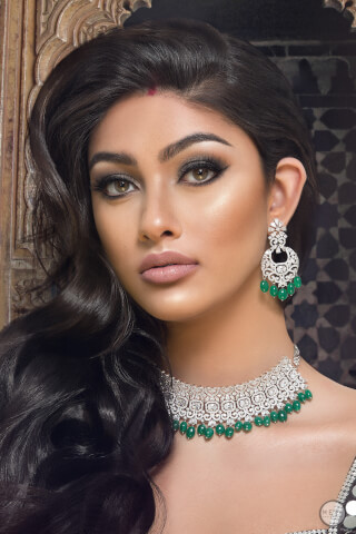 A woman wears elegant diamond and emerald jewelry, promoting sophistication and beauty in a close-up editorial style shot.