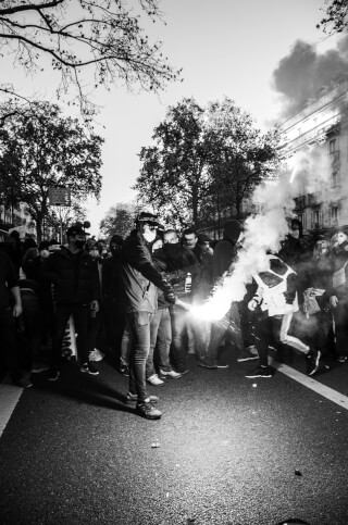 A black and white photo of people protesting in a city street with one person holding a flare.