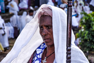 A woman with a headscarf and cross necklace attends an outdoor religious event.