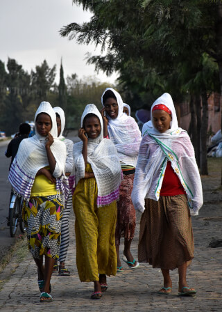 A group of women in headscarves walk together on a sidewalk in a street.