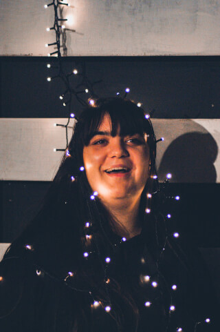A smiling woman wrapped in glowing fairy lights in a festive and cheerful setting. Perfect for social media or holiday campaigns.