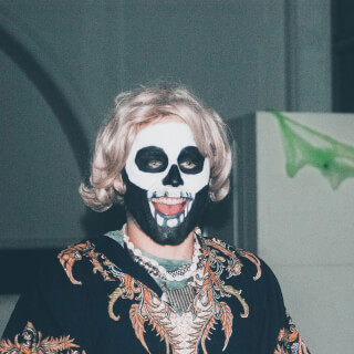 A person with skeleton face paint and a blonde wig celebrates Halloween in a festive costume.