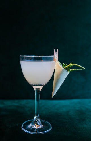 A refreshing cocktail garnished with samphire is artfully presented in a clear glass.