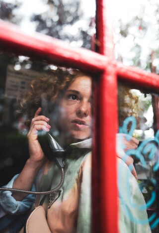 A young woman with freckles uses a vintage telephone inside a red phone booth.