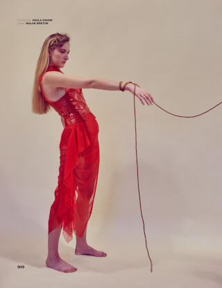 A woman in a red dress and corset poses in a studio with a rope.