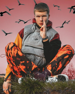 A young man in streetwear poses outdoors against a backdrop of birds in flight.