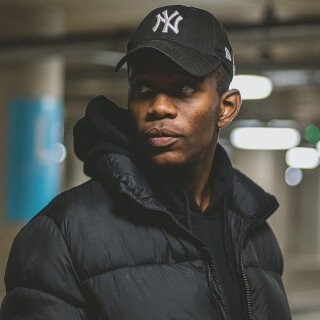 A man wearing a New York Yankees cap and a black puffer jacket looking away in an indoor parking garage.