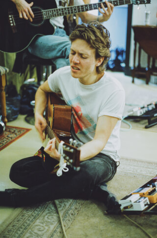 A musician plays acoustic guitar with band in a relaxed, warm-toned setting, perfect for music or lifestyle campaigns.