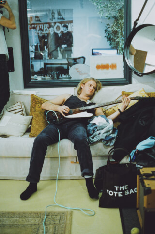 A relaxed man lounges on a couch, casually playing a guitar in a cozy indoor setting.
