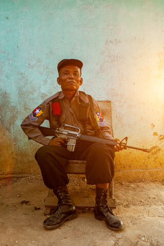 A man in uniform sitting and holding a rifle outdoors.