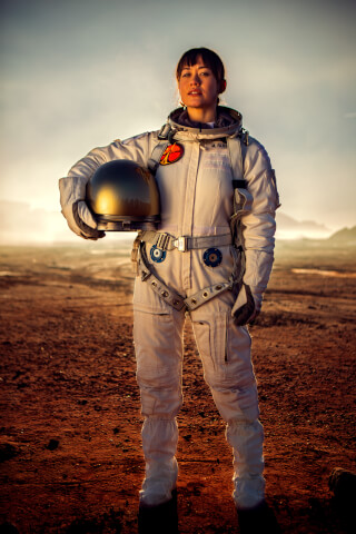 A female astronaut confidently stands on Mars holding her helmet, ready for exploration and scientific discovery.
