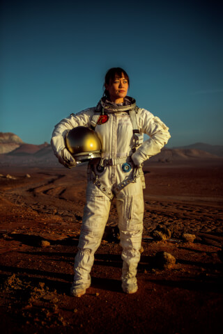 A determined female astronaut in a spacesuit stands on Mars, holding her helmet, exuding strength and ambition.