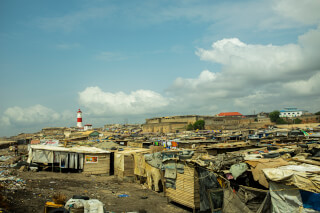 An overview of shacks in a slum, featuring a red and white lighthouse under a cloudy sky.