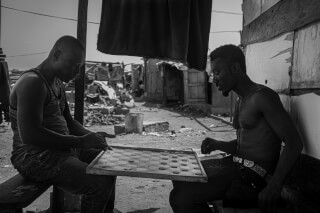 Two men are intensely playing checkers in a black and white outdoor street scene.