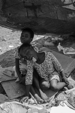 Two young children sit under shelter in a black and white image, seeking refuge from the elements.