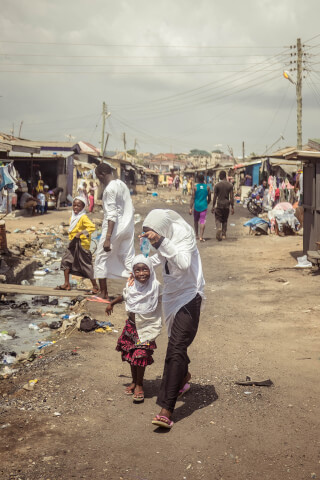A group of people, including a woman and children, walk down a dirt road in a developing country.