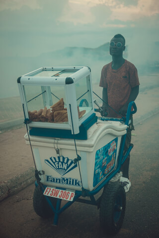 A man stands beside his food cart, selling snacks on a street.
