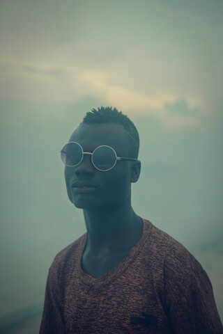 Portrait of a man in sunglasses against a muted, cloudy background, creating a contemplative and stylish image.