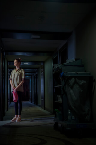 A young hotel maid stands in a hallway with her cleaning cart in this commercial image.