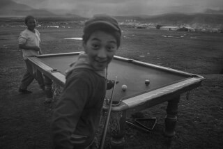 Two boys enjoy a game of pool in a rural setting, captured in striking black and white.