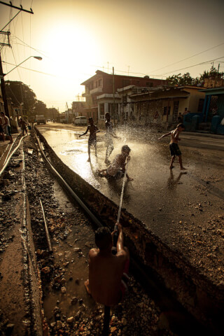 Children play with a water hose on a street, creating a fun and energetic scene with warm tones.