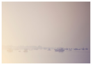 A hazy view of boats on calm water near the coastline in Vietnam. Soft, muted tones create a tranquil scene.