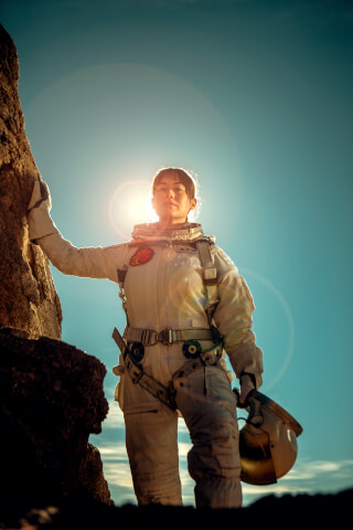 An astronaut stands confidently in a spacesuit against a rocky landscape and bright sky, looking determined and ready for exploration.