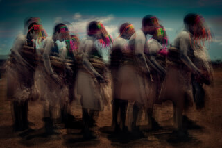 A group of people in traditional African dress dance in a field, with motion blur conveying movement and cultural heritage.